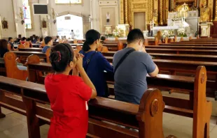 Hombres y mujeres católicos se arrodillan y rezan dentro de la Catedral de Antipolo en Filipinas. Crédito: junpinzon / Shutterstock.